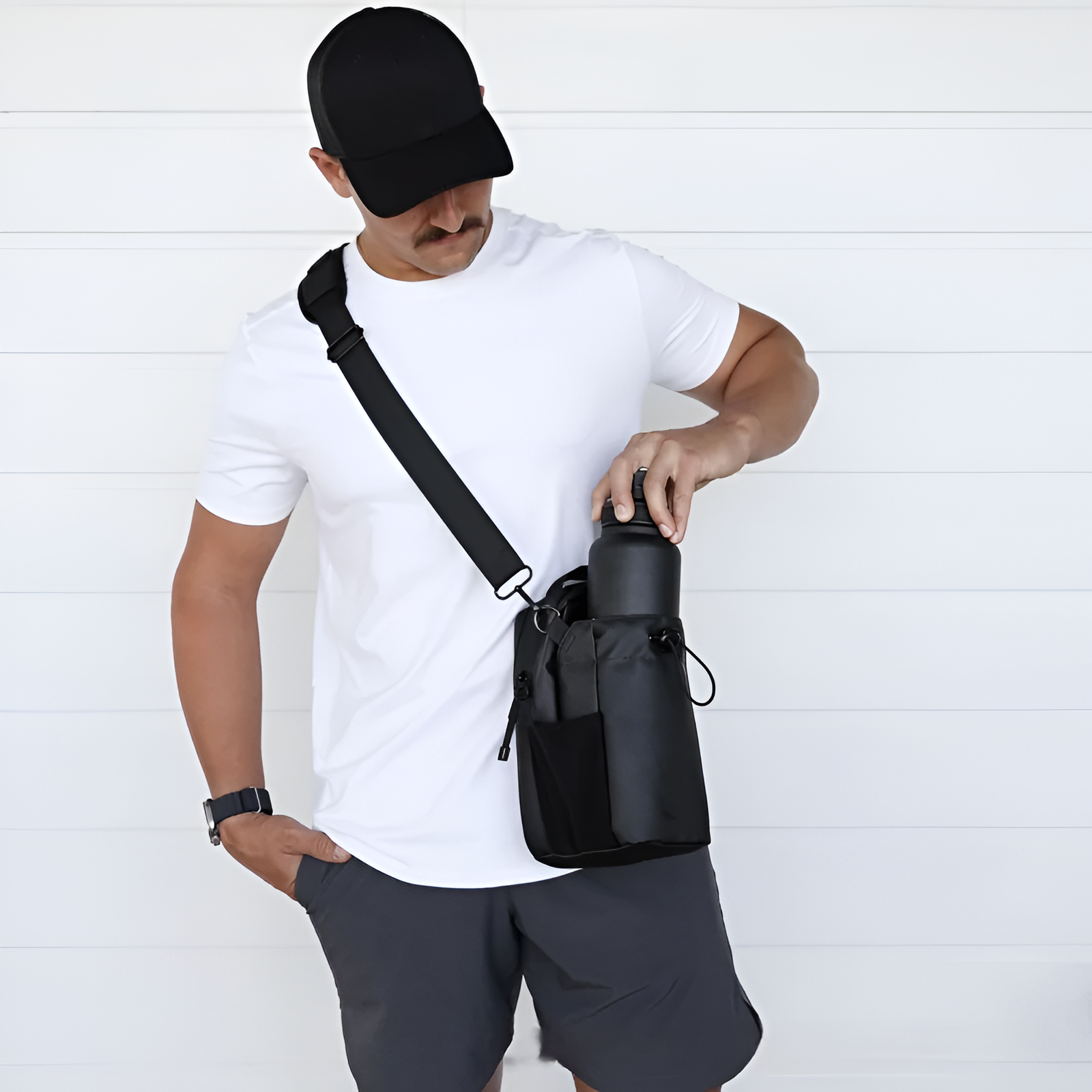Person wearing a black cap and carrying a black crossbody bag against a white background